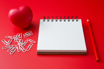 Notebook, pencil, paper clip, heart shaped ball  on a red background and copy space