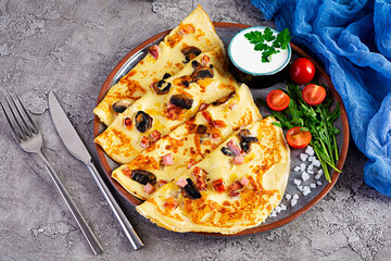 Delicious pancakes with mushrooms, ham and cheese, arugula, tomatoes and sour cream on a wooden background