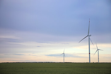 Fototapeta na wymiar Beautiful view of field with wind turbines in evening. Alternative energy source