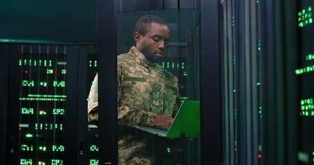 African Americam army man in camouflage costume opening server and controlling. Male typing on laptop computer and checking data in control center. Work at secret information in army. Digital concept.