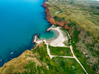 Bolata Beach, Cape Kaliakra, on the northern coast of Bulgaria. The high steep banks of a reddish hue are in harmony with the greenery of grass and the endless blue sea. View from drone.