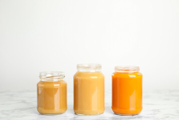 Healthy baby food in jars on marble table against white background