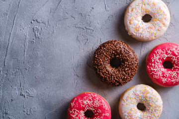 Chocolate, pink and vanilla donuts with sprinkles, sweet glazed dessert food on concrete textured background, top view copy space
