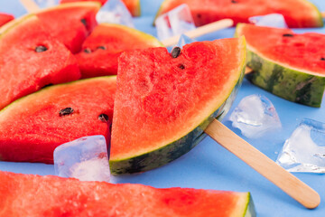 Watermelon slices on sticks with ice cubes. Fresh watermelon popsicles on blue background.