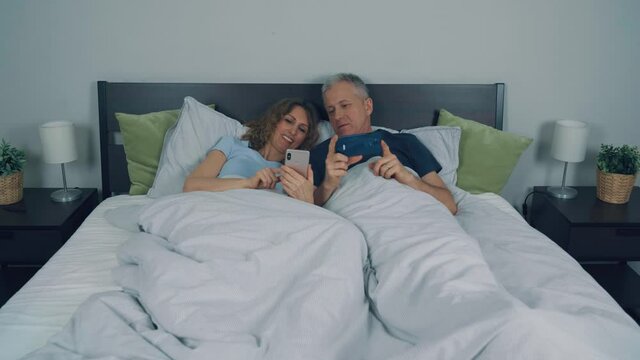 People, a man and a woman are lying in bed and looking at the phone.