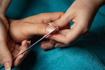 A girl with beautiful nails saws nails with a sawn to a young man at home in the evening. Homemade amateur manicure.