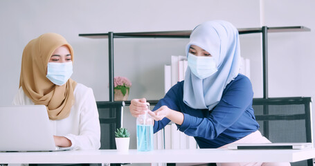 Muslim businesswomen wear protective masks and clean hands with sanitizer alcohol gel during work in office.
