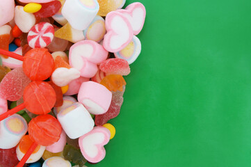 Mixed colorful fruit candies and jellies on green background with room for text