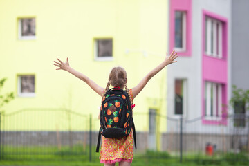 Happy schoolgirl with pigtails going to school. Girl raising arms with backpack, back view. Starting new school year. Concept of primary school education. Back to school.