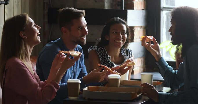 Happy multiracial business team people students laughing eating takeaway pizza together in cafe indoor, cheerful diverse staff friends group having fun share lunch food meal enjoy party sit at table