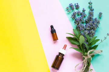 Two herbal facial serums with lavender extract and bouquet of fresh aromatic lavender on multicolored background top view. Copy space for your design. Skin care concept.