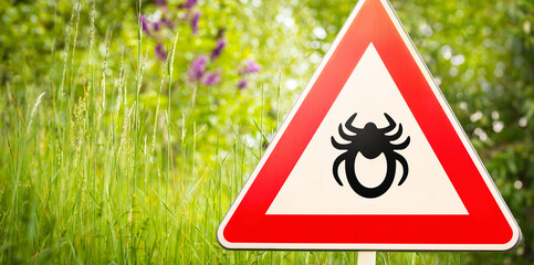 Attention sign with symbol of a tick in front of a nature background with high grass