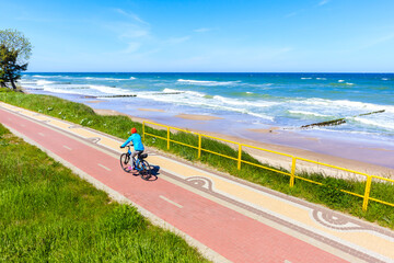 Young woman cyclist riding bike along beautiful beach with near Kolobrzeg town, Baltic Sea coast, Poland
