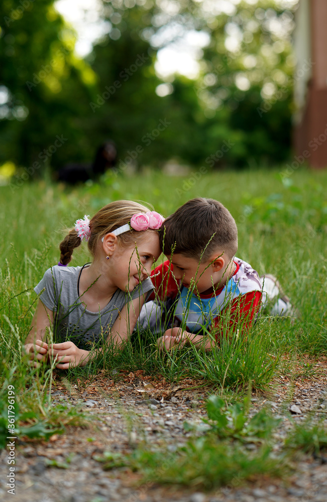 Wall mural cute little girl and boy lying together in grass on lawn