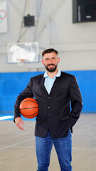 A young man with beard in a blazer and jeans with a basketball in his hands