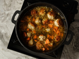 Cooking soup with meatballs cutlets and vegetables in big pan pot on home kitchen background by chef hands. Copy space, closeup. Homemade food recipe concept.