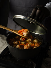 Cooking soup with meatballs cutlets and vegetables in big pan pot on home kitchen background by chef hands. Copy space, closeup. Homemade food recipe concept.