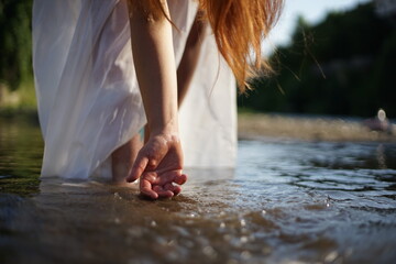 A girl/ young woman with red hair and a white dress. She is playing with water. The photo is taken in a rural scene. The weather is sunny, yet the light is soft and warm.