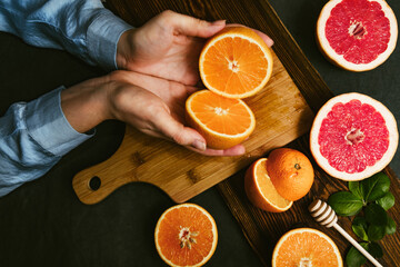 Top view of hands holding juicy oranges cut in halves. Citrus fruit dark background. Preparing detox citrus juice or lemonade rich in vitamin c