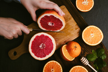 Top view of hands cutting fresh grapefruit in halves on wooden board. Preparing detox citrus juice rich in vitamin c for immunity boost