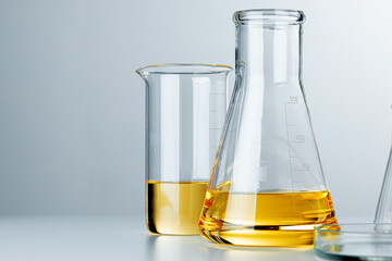 Laboratory glassware with yellow oily liquid on grey background