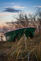 Fototapeta na wymiar Green boat anchored on a grass-covered sand dune during sunset, Latvia.