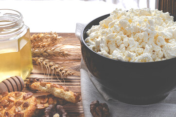Healthy food: homemade cheese in a black round plate stands on a wooden table next to a jar of honey
