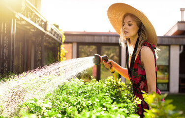 Pretty young girl in a hat watering plants with a garden hose in the garden in summer, photography...