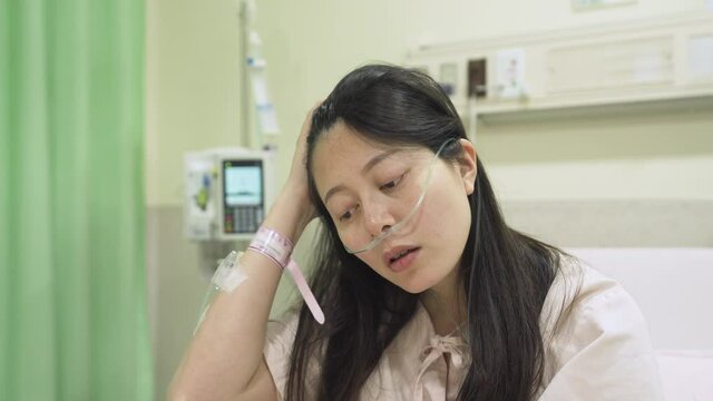 portrait asian lady having a miscarriage is staring blankly, feeling sorrowful and depressed. patient with tube on face and arm flipping hair is still dazed by the fact that she has lost her child.