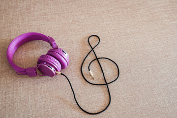 Purple headphones with cord shaped in G clef in light brown background