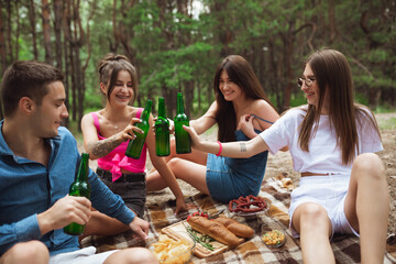 Happiness. Group of friends clinking beer bottles during picnic in summer forest. Lifestyle, friendship, having fun, weekend and resting concept. Looks cheerful, happy, celebrating, festive.