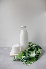 A bottle of milk on a net background, next to a mug and a towel with a green floral print, minimalism