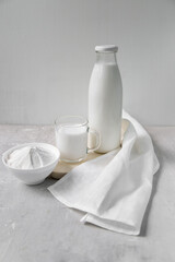 Milk in a bottle, next to a mug with milk and a bowl with milk powder on a light background