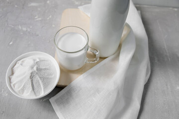 Milk in a bottle, next to a mug with milk and a bowl with milk powder on a light background