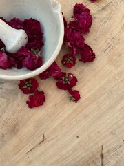 White mortar and pestle filled with red dry roses on a wooden light table