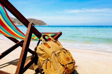 open sea, A deck chair on the sandy shore of a tropical beach. stylish brown backpack standing nearby. traveler, freelancer