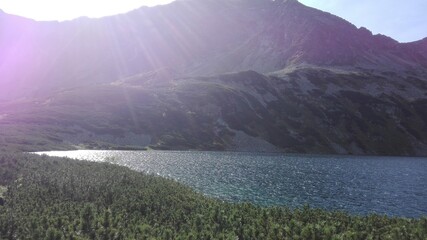Landscape with silent blue lake, surrounded by small green forest, green mountain in the background © Kamil