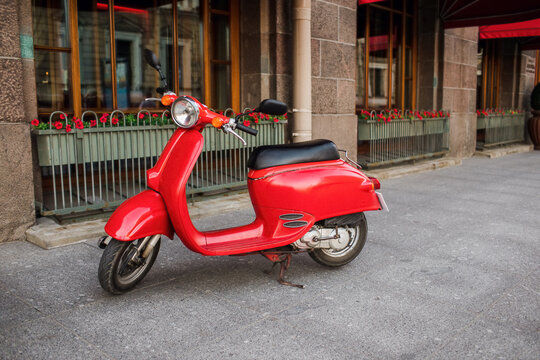Red vintage scooter parked on sidewalk of empty city street
