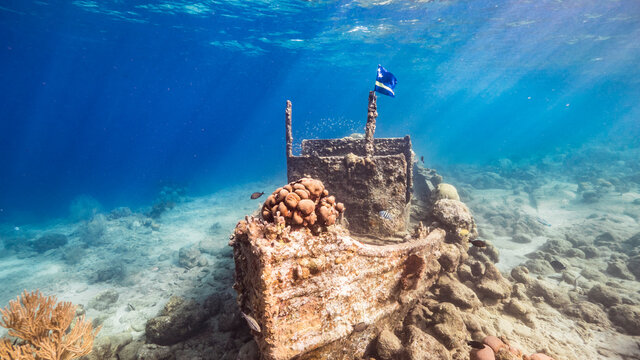 Ship wreck "Tugboat" in  shallow water of coral reef in Caribbean sea with  Curacao Flag, view to surface and sunbeams 

