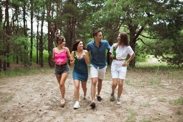 On the way. Group of friends walking down together during picnic in summer forest. Lifestyle, friendship, having fun, weekend and resting concept. Looks cheerful, happy, celebrating, festive.