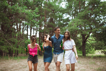 Fototapeta premium On the way. Group of friends walking down together during picnic in summer forest. Lifestyle, friendship, having fun, weekend and resting concept. Looks cheerful, happy, celebrating, festive.