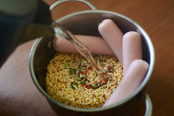 Instant vermicelli and sausages in a pan. Cooking, adding boiling water. Trashy, unhealthy food.