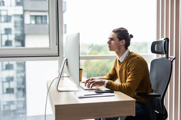 happy young businessman working on desktop computer at his desk in modern bright startup office interior