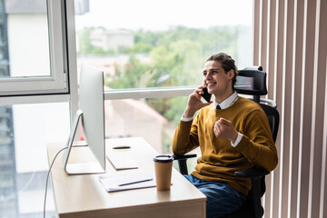 Young businessman talking on phone and working on computer in office