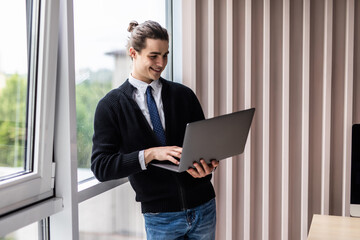 Portrait of handsome businessman smiling while using laptop in office
