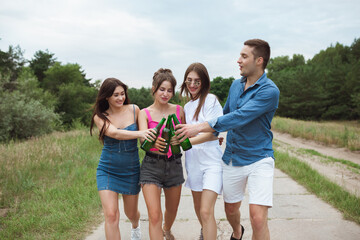 On the way. Group of friends clinking beer bottles during picnic in summer forest. Lifestyle, friendship, having fun, weekend and resting concept. Looks cheerful, happy, celebrating, festive.