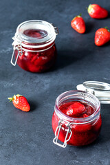 Jars of homemade strawberry jam with ripe strawberries on a dark background
