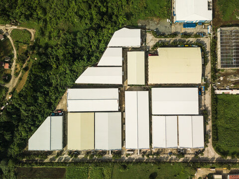 Top view of a large industrial compound with beige roofs surrounded by farmland and trees.