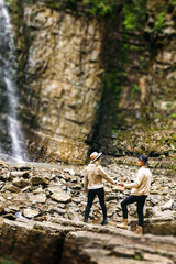 Young and beautiful couple at the mountain waterfall - Happy tourists visiting mountains. Lovestory. Tourists in hats. Military fashion.