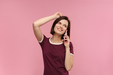 Fototapeta premium Young people working with mobile devices. Portrait of cute happy brunette woman wearing t-shirt talking on mobile phone and smiling isolated over pink background. Copy space.